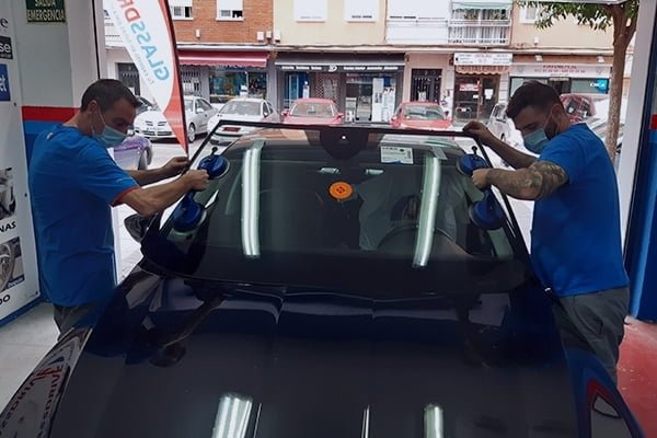 Dos técnicos colocando un parabrisas nuevo en un coche